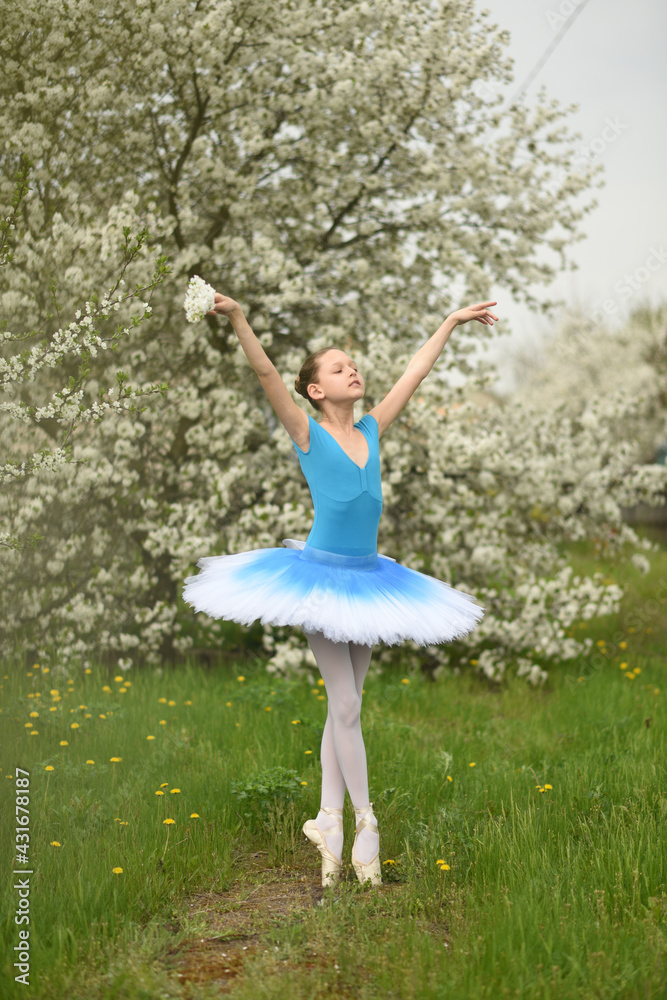 Ballerina in pointe shoes and a ballet tutu in the park. Ballet positions. Beautiful child in the park in spring in flowering trees
