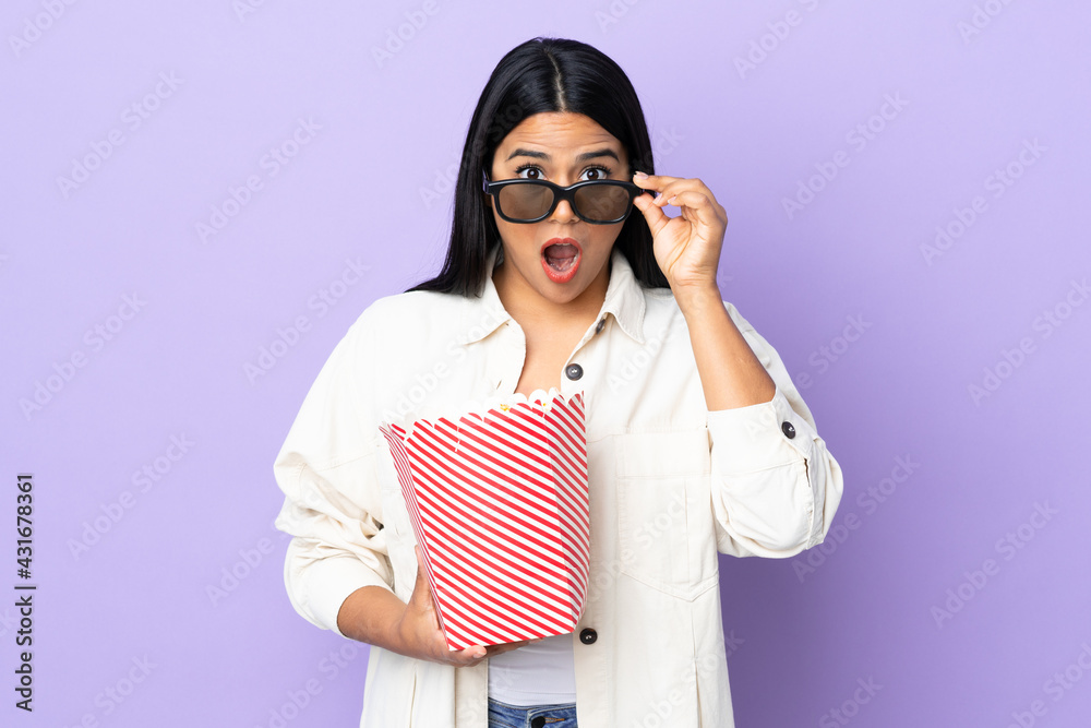 Young latin woman woman isolated on white background surprised with 3d glasses and holding a big bucket of popcorns Young latin woman woman isolated on white background surprised with 3d glasses and holding a big bucket of popcorns