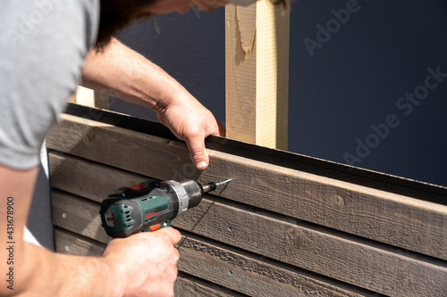 tough construction worker applies wooden siding to a garage and drills screws