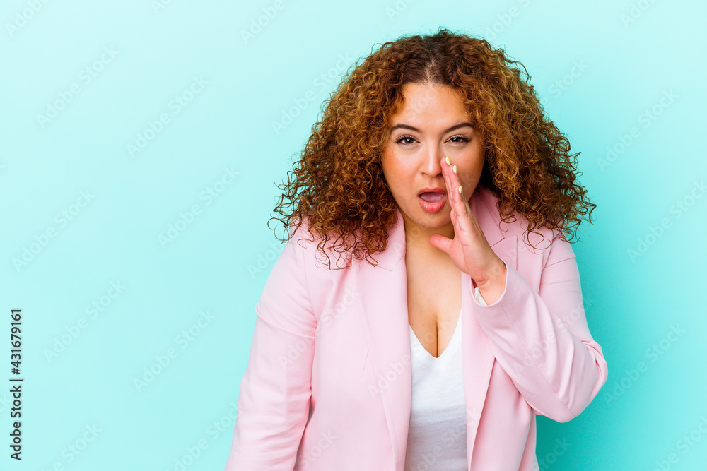 Young latin curvy woman isolated on blue background is saying a secret hot braking news and looking aside