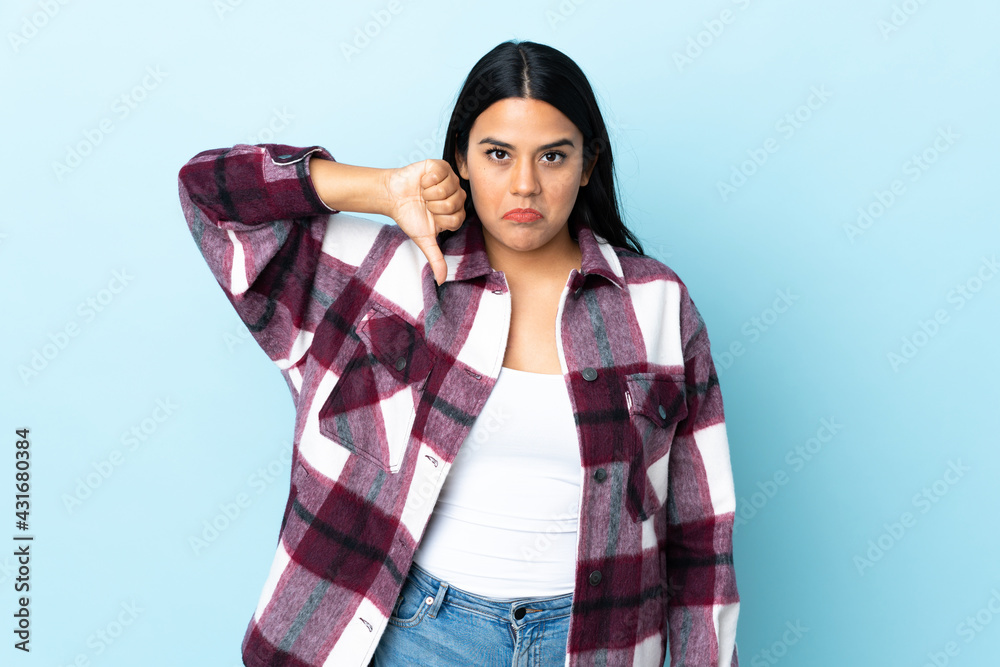Young latin woman woman isolated on blue background showing thumb down with negative expression Young latin woman woman isolated on blue background showing thumb down with negative expression