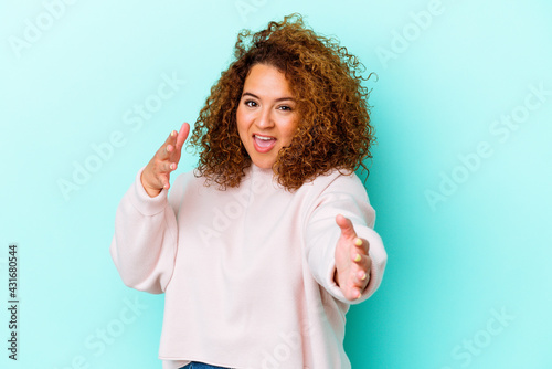 Young latin curvy woman isolated on blue background feels confident giving a hug to the camera.