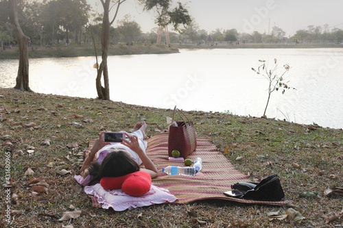 Woman relax on mat and take photo at the park near the pond
