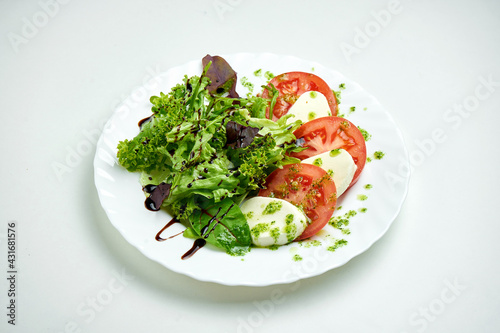 Classic Italian caprese salad with tomatoes, mozzarella, mix salad and pesto sauce in a white plate on a white plate