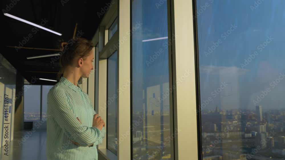 Portrait of smiling woman looking at cityscape through window of skyscraper. Summer time, sunset. Relax, leisure time, entertainment, success, opportunity, sightseeing, discover and future concept Portrait of smiling woman looking at cityscape through window of skyscraper. Summer time, sunset. Relax, leisure time, entertainment, success, opportunity, sightseeing, discover and future concept