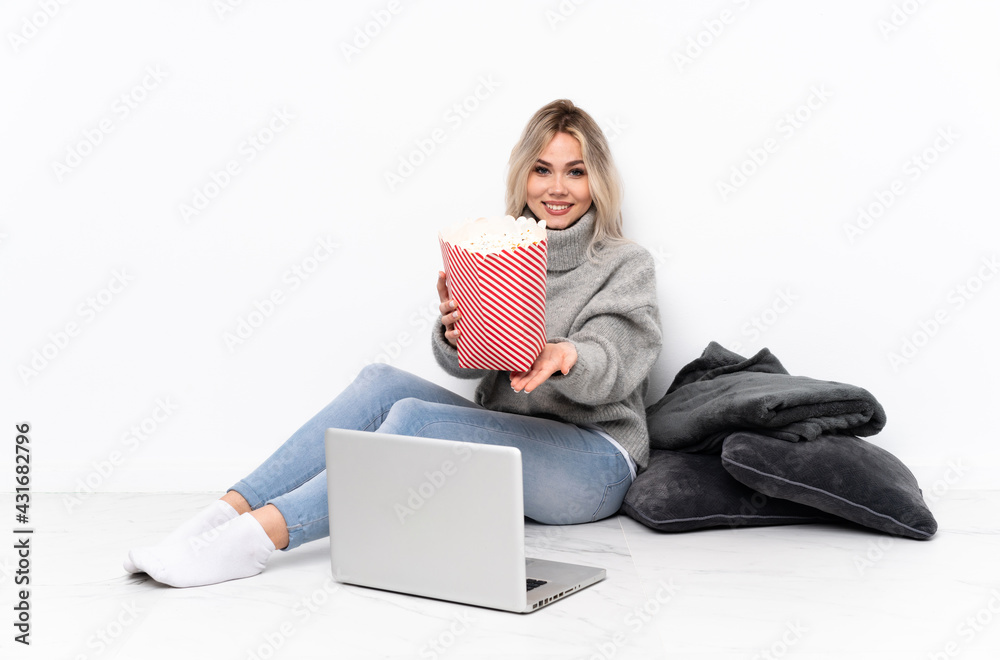 Teenager blonde girl eating popcorn while watching a movie on the laptop holding copyspace imaginary on the palm to insert an ad Teenager blonde girl eating popcorn while watching a movie on the laptop holding copyspace imaginary on the palm to insert an ad