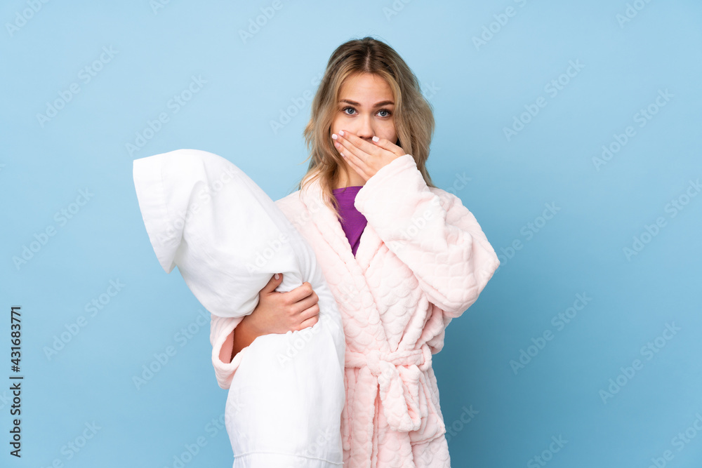 Teenager Russian girl in pajamas isolated on blue background covering mouth with hands Teenager Russian girl in pajamas isolated on blue background covering mouth with hands