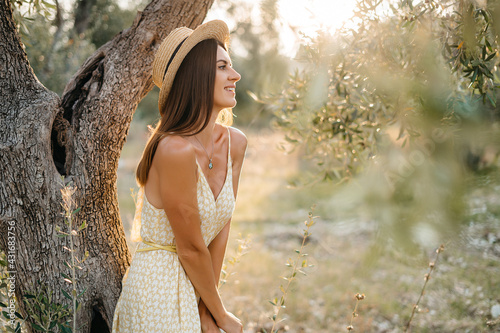 portrait of beautiful young brunette woman in straw hat at sunset in olive garden. Travel to Italy, summer vacation