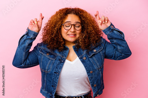 Young latin curvy woman isolated on pink background crossing fingers for having luck