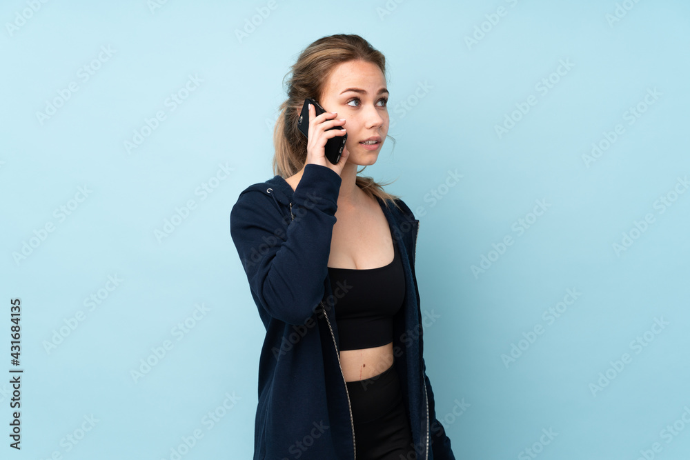 Teenager Russian girl holding mat isolated on blue background keeping a conversation with the mobile phone with someone Teenager Russian girl holding mat isolated on blue background keeping a conversation with the mobile phone with someone