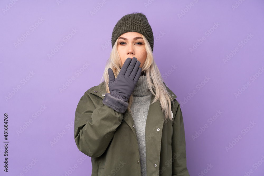 Teenager blonde girl with winter hat over isolated purple background yawning