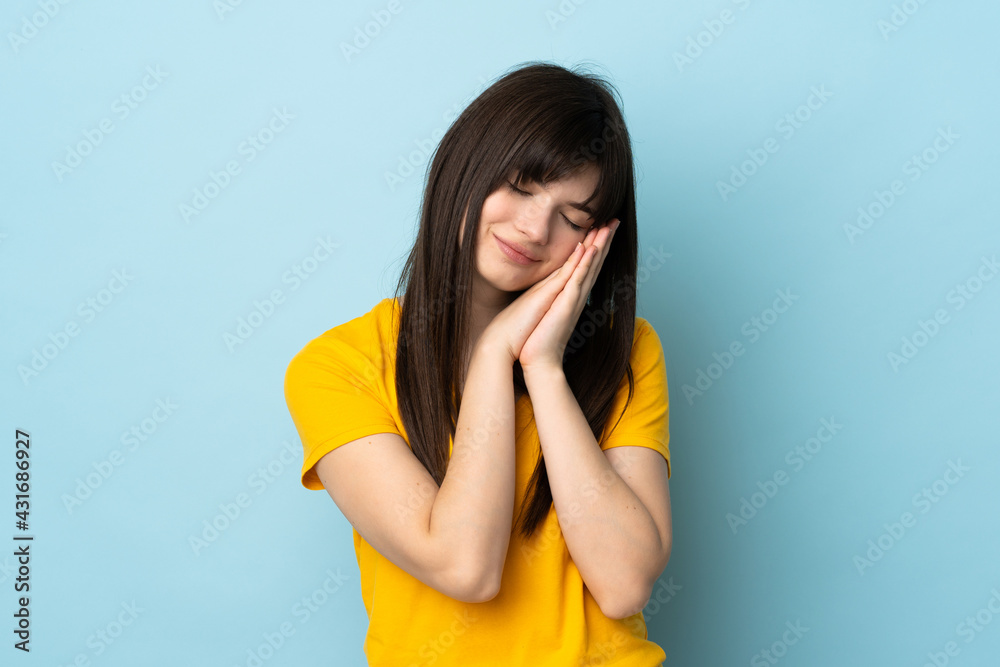 Teenager Ukrainian girl isolated on blue background making sleep gesture in dorable expression