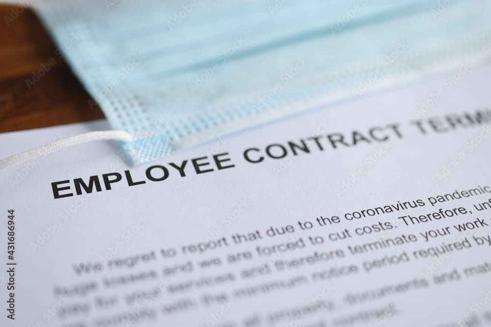 Termination of employment contract due to coronavirus pandemic, along with protective mask lies on table Termination of employment contract due to coronavirus pandemic, along with protective mask lies on table