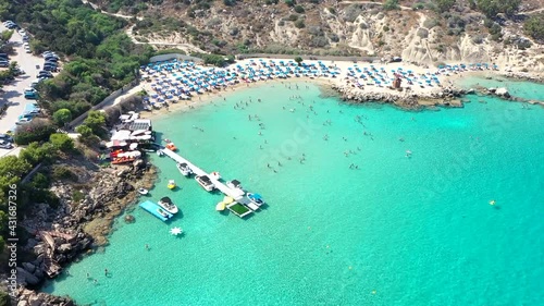 Sand and stone Beach with crystal blue water from drone. People are jumping and swimming 