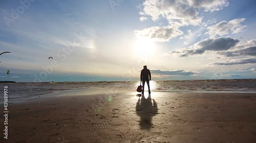 A man with a guitar stands with his back on the beach and looks at the waves of the ocean.