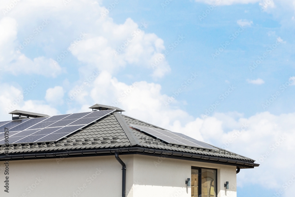 Solar panels on the roof of the house. Renewable solar energy. Blue sky and white clouds. Copy space for text Solar panels on the roof of the house. Renewable solar energy. Blue sky and white clouds. Copy space for text