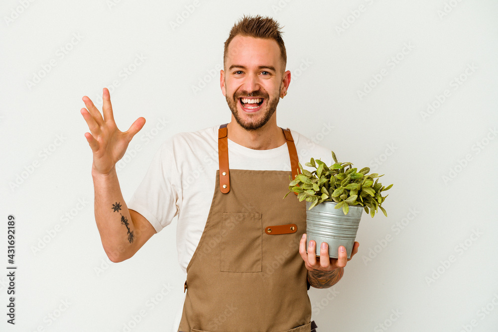 Young gardener tattooed caucasian man holding a plant isolated on white background receiving a pleasant surprise, excited and raising hands. Young gardener tattooed caucasian man holding a plant isolated on white background receiving a pleasant surprise, excited and raising hands.