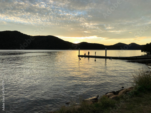 Sunset over water with mountain, people, pelicans and jetty silhouette