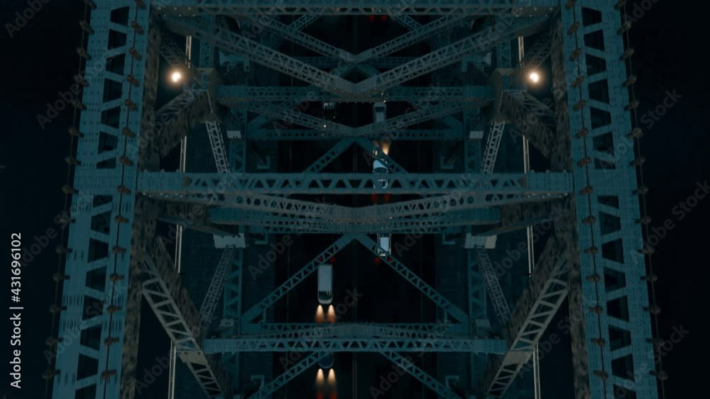 The view from above a steel-structured suspension bridge at night, looking down on the moving traffic below. The view from above a steel-structured suspension bridge at night, looking down on the moving traffic below.