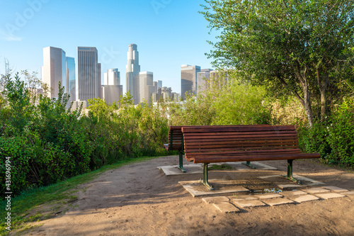 An empty bench in a Los Angeles park with a view of Downtown skyscrapers. Morning in summer. Los Angeles, USA - 16 Apr 2021