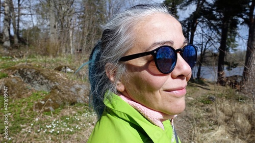 Photo of a woman's face with ponytail hair, sunglasses, a pink sweatshirt and a light green jacket