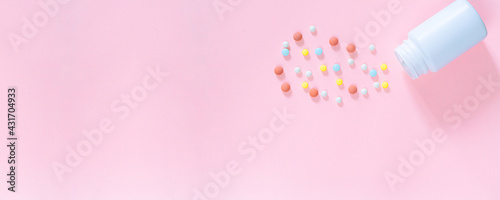 Multicolored tablets, pills, capsules in plastic bottle on pink background, copy space. Heap of assorted various medicine tablets and pills, vitamin and nutritional supplements concept.