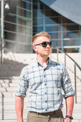 A young blond man in sunglasses stands on the steps of the Walt Disney Concert Hall. Business style in a trendy building, Los Angeles