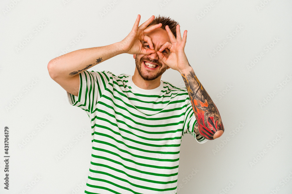 Young tattooed caucasian man isolated on white background showing okay sign over eyes Young tattooed caucasian man isolated on white background showing okay sign over eyes