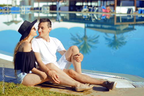  A sunny day, a man and a girl enjoy the rest. Travel. Against the background of palm trees and houses. Couple at the hotel with a pool. The concept of relaxation and travel. Kiss
