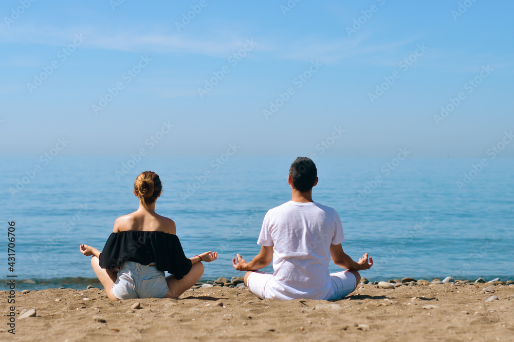 A couple is engaged in yoga on the beach against the background of the sea. Health and sports. A woman and a man on the shore of the ocean are meditating and relaxing. Summer and travel. A couple is engaged in yoga on the beach against the background of the sea. Health and sports. A woman and a man on the shore of the ocean are meditating and relaxing. Summer and travel.