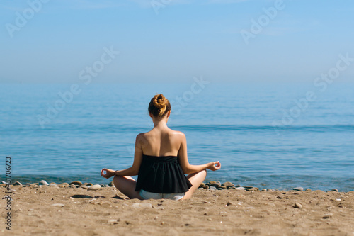 A beautiful girl is engaged in yoga on the beach against the background of the sea. Health and sports. A woman on the ocean shore meditates and relaxes. Summer and travel.