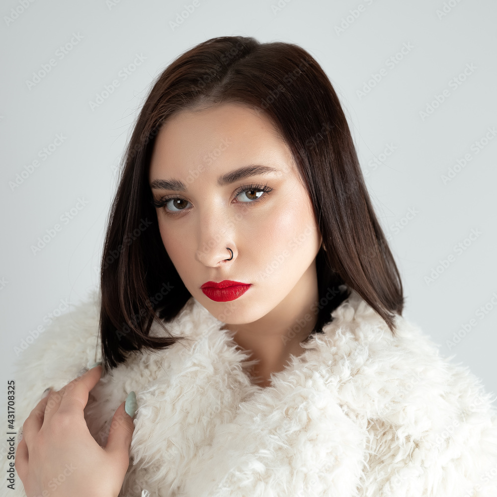 Young woman with great shapes brows, long eyelashes and red lips. Brunette posing on white wall