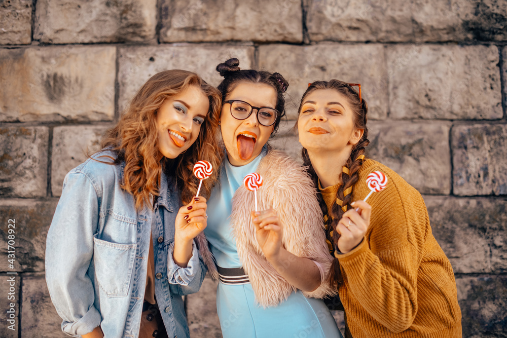 Three pretty girls eat sweets and drink juices and drinks outside on a nice summer day. A group of teenagers are walking in the summer, dressed in fashionable clothes, eating ice cream.