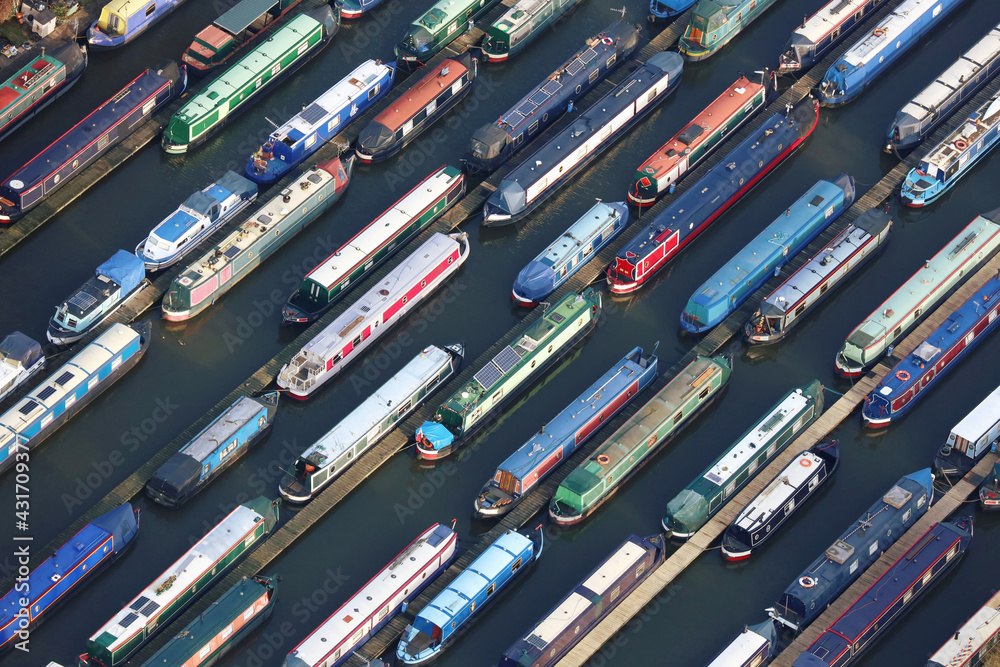 An aerial photograph taken from a helicopter of a large canal narrow boat marina in Britian. Many colourful pleasure boats are moored in lines making an interesting striped repeating pattern. An aerial photograph taken from a helicopter of a large canal narrow boat marina in Britian. Many colourful pleasure boats are moored in lines making an interesting striped repeating pattern.