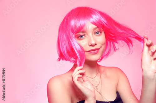 The girl in a pink wig, on a pink background, is happy, grimaces, smiles. Bright photo of a teenager, smart, party, dance. Anime pink cute girl