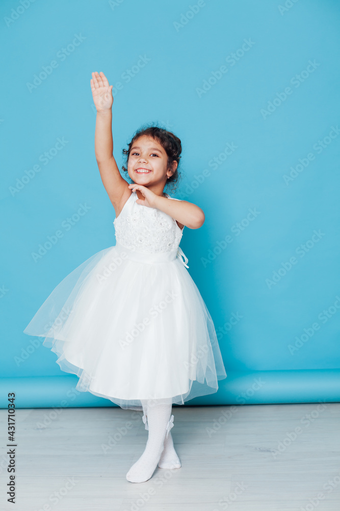 Beautiful little girl dances to the song in a white dress on a blue background Beautiful little girl dances to the song in a white dress on a blue background