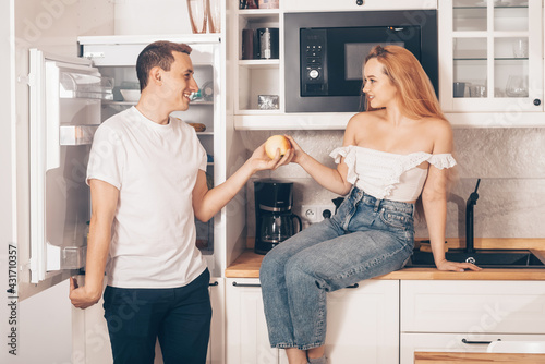 The guy and the girl in the kitchen. Loving couple at home. The man feeds and gives the woman an apple. The couple eats healthy food. Useful ration. Prepare breakfast together, morning.