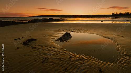 Pool of water reflects sunset on sand beach