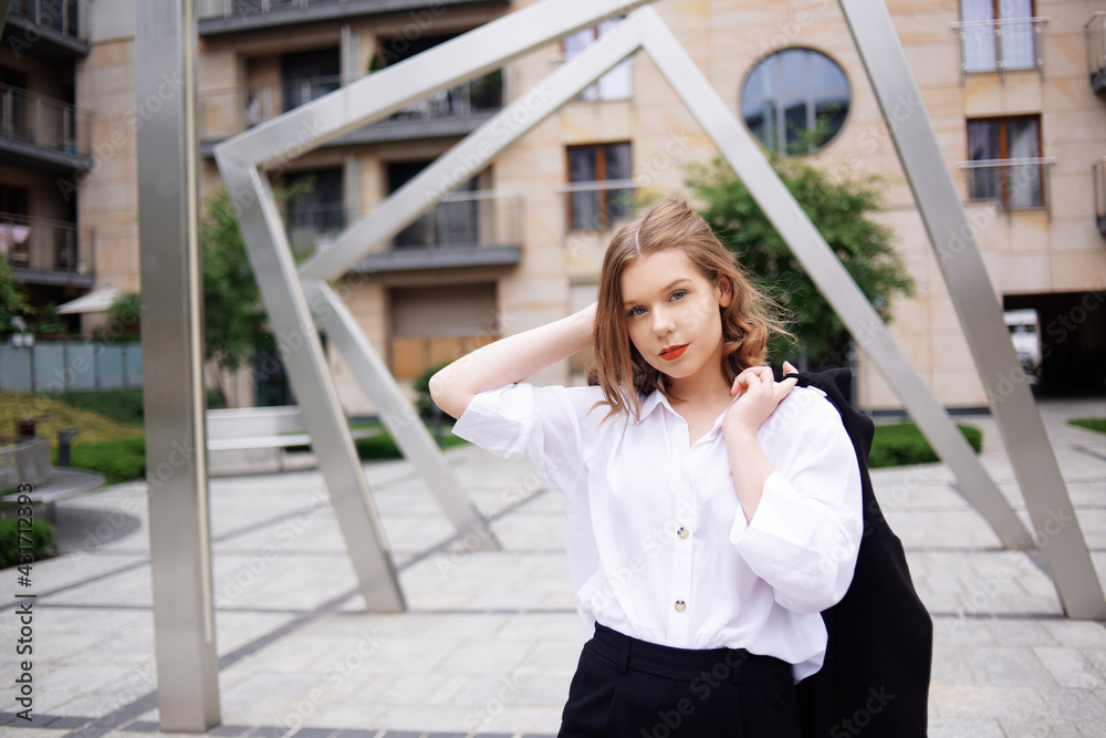 Student, manager, realtor, girl in a white shirt on the background of the building posing. Beautiful blonde with short hair. Model with red lips and a black jacket.