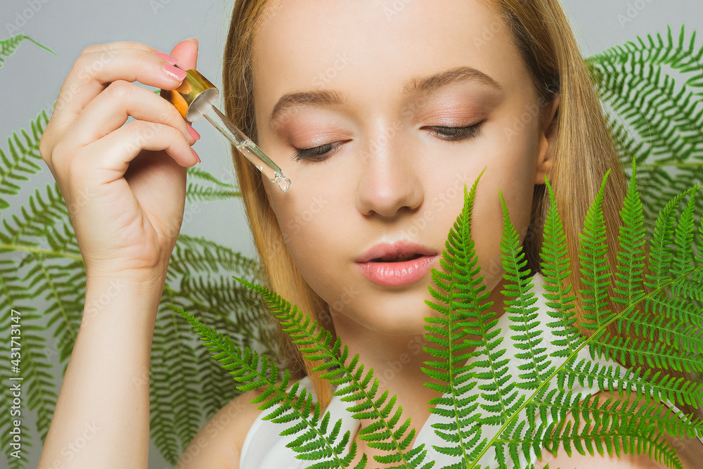 Girl on the background of tropical leaves natural cosmetics and medicines. The model holds a bottle and oil for the face and applies it to the skin. Bottle with a pipette.