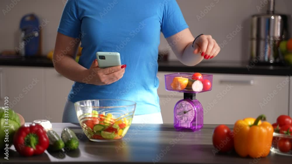Midsection of healthy eating woman using kitchen scales to weigh vegetables and smartphone with weight loss application to calculate calorie content of dish. Slimming woman counting calories