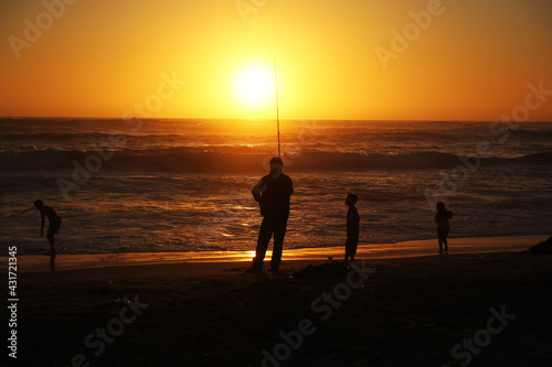 Silhouette of a fisherman with children on a beach during a sunset