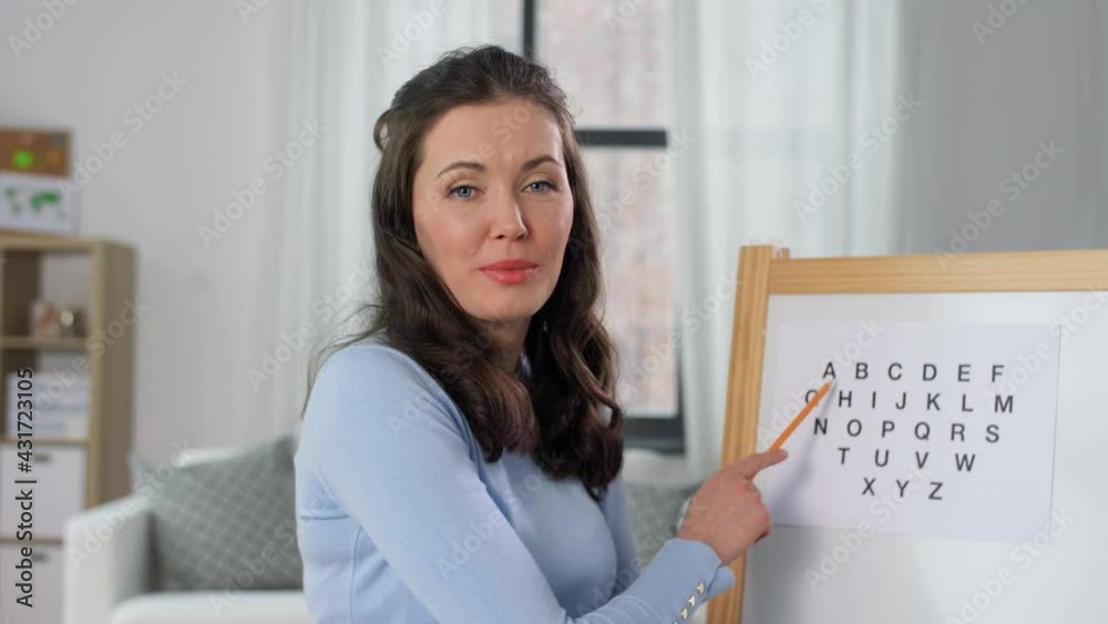 distant education, primary school and teaching concept - female teacher with alphabet having online class at home distant education, primary school and teaching concept - female teacher with alphabet having online class at home