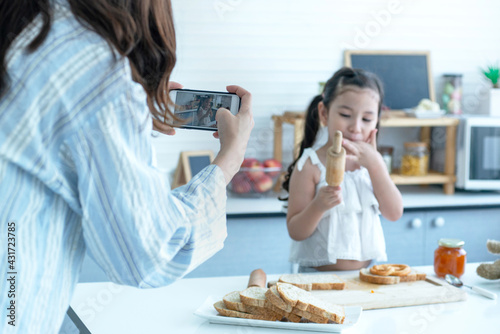 Mom taking pictures of her daughter or recording a vlog, making video call on phone having fun together in kitchen