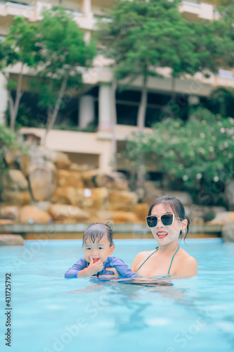 Asian mother and little son enjoying swimming in a swimming pool in summer vacation.