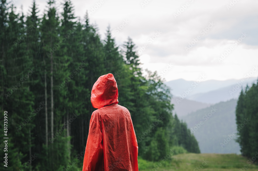 Person in a red raincoat stands on the rain in the mountains against backdrop of a beautiful landscape with coniferous trees and fog. Hiker in the Carpathian Mountains in the Rain. Copy space Person in a red raincoat stands on the rain in the mountains against backdrop of a beautiful landscape with coniferous trees and fog. Hiker in the Carpathian Mountains in the Rain. Copy space