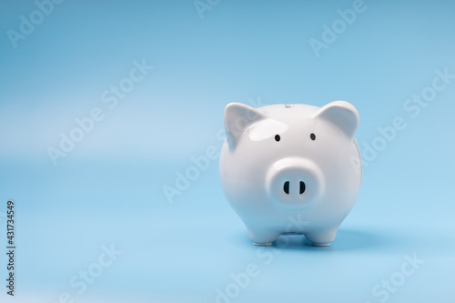 Single white piggy banks on blue background with copy space. Concept saving money, investment, save money in future, and finance.