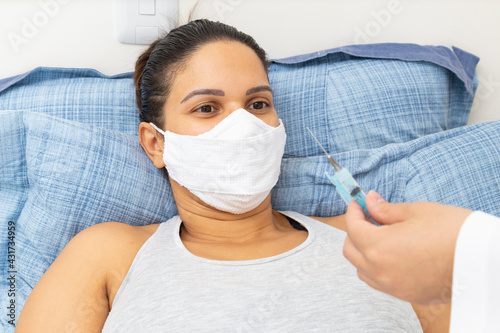 Foto Patient in bed wearing a mask and looking at a syringe.