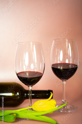 two wine glasses with wine bottle, pink background, tulips