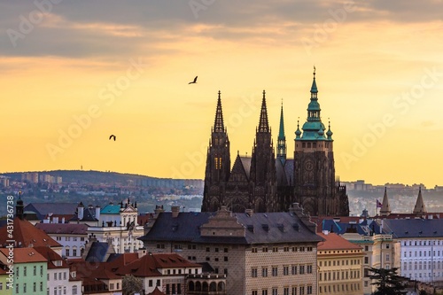 Prague, Czech Republic - May 3 2021: View of the Prague castle during morning sunrise. Orange and blue sky in the background and two birds flying by.